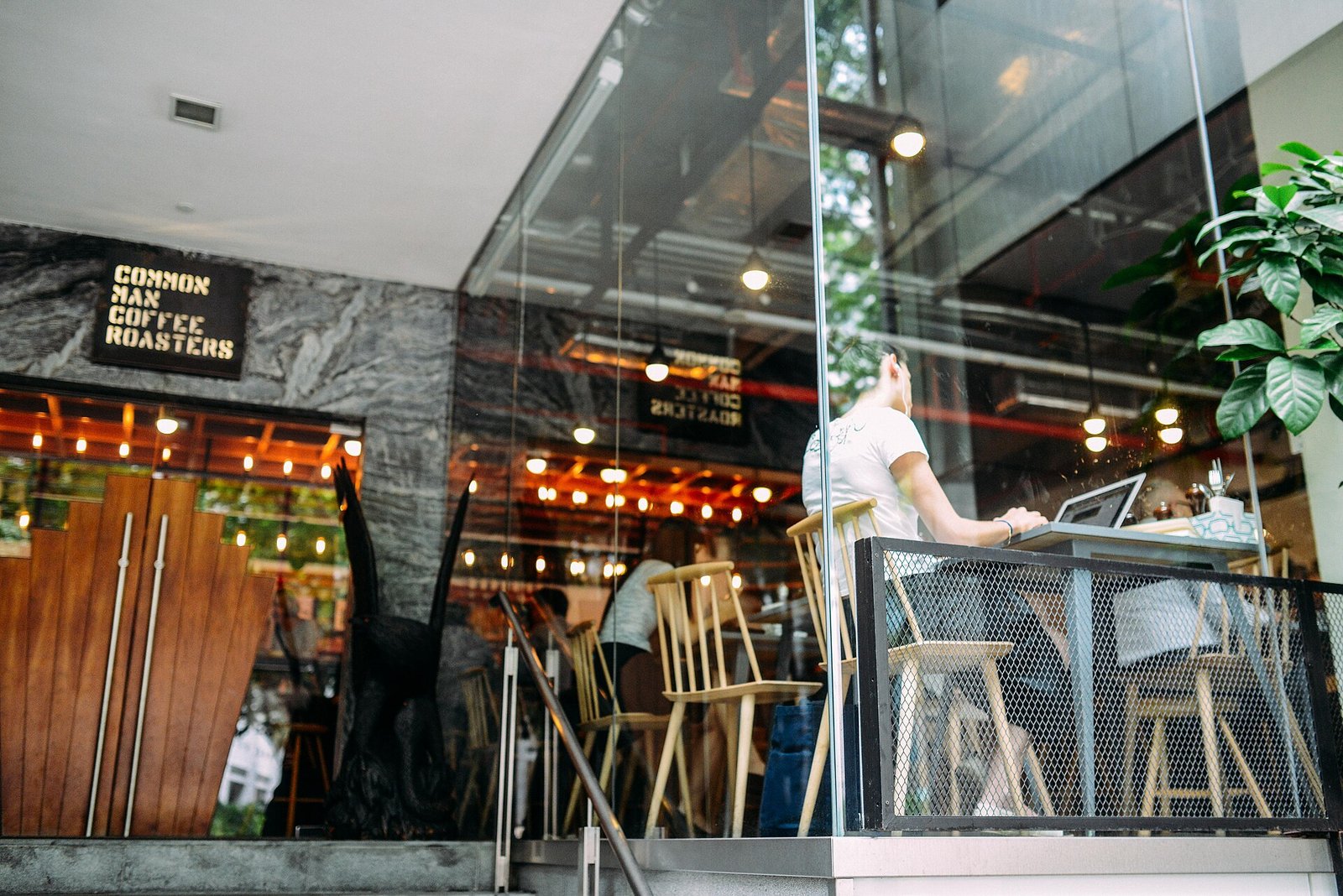 Interior do Common Man Coffee Roasters em Singapura, com balcão de café e mesas de madeira