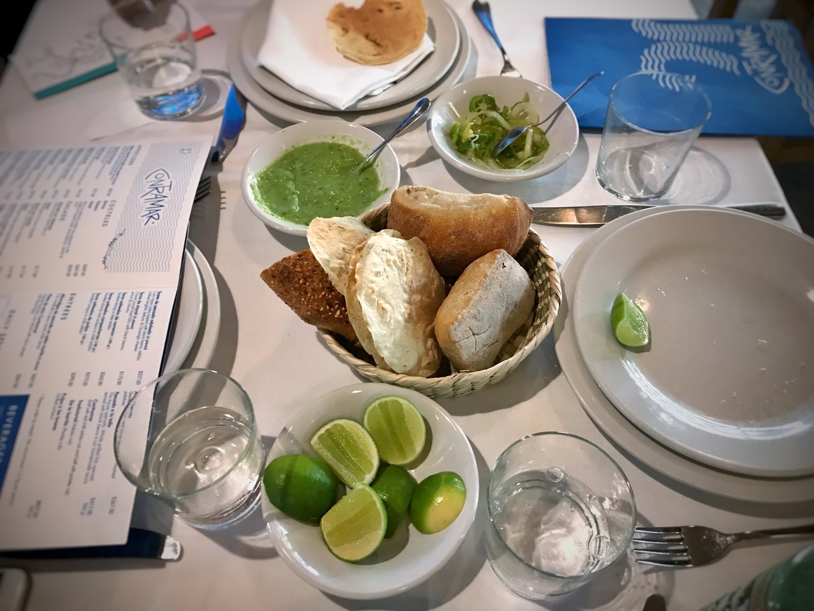 Mesa posta no restaurante Contramar, com pães, limões e o menu do restaurante
